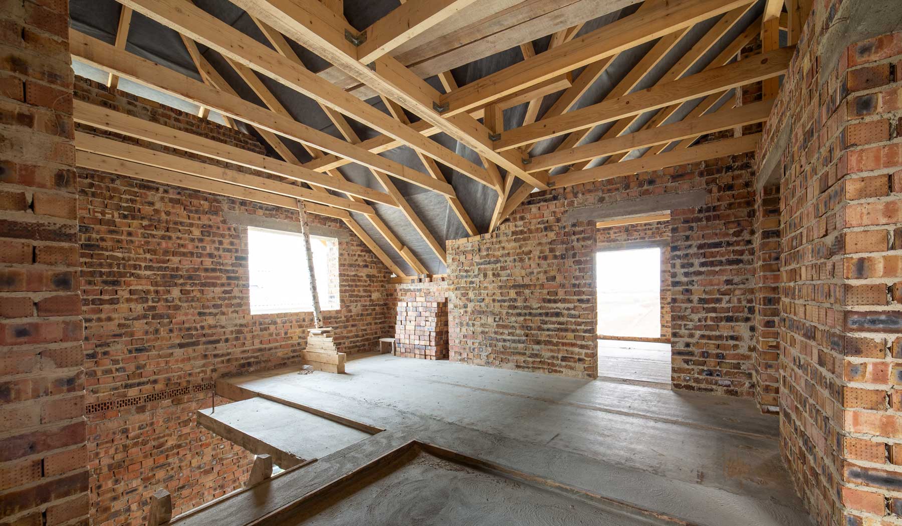 Loft conversion under construction with exposed timber roof trusses, brick walls and new floor structure during a residential home extension project in Surrey and Hampshire.