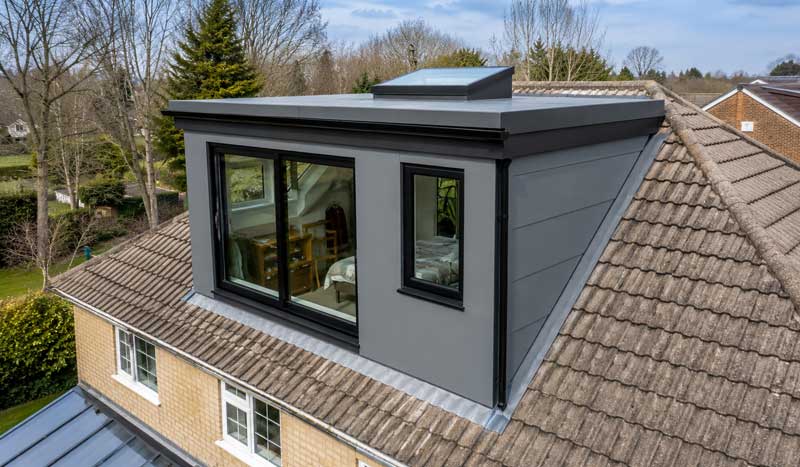 Modern rear dormer loft conversion with grey composite cladding, flat roof skylight, large anthracite-framed windows and a spacious loft bedroom, adding extra living space to a UK suburban home.