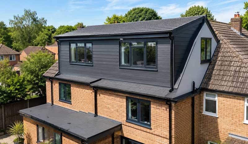 Hip-to-gable loft conversion with dark grey cladding, modern roof extension, anthracite-framed windows and expanded upper-floor living space on a detached UK brick home.
