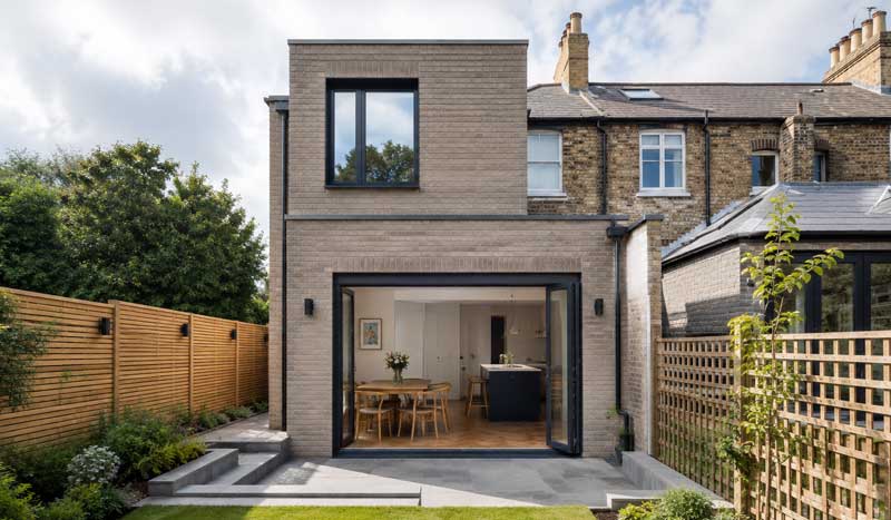 Modern double-storey house extension with light brick exterior, black aluminium framed sliding doors, landscaped garden, and contemporary rear home renovation in a UK residential property.