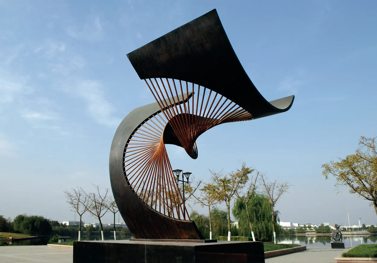 Monumental abstract metal sculpture installed beside a landscaped lake.