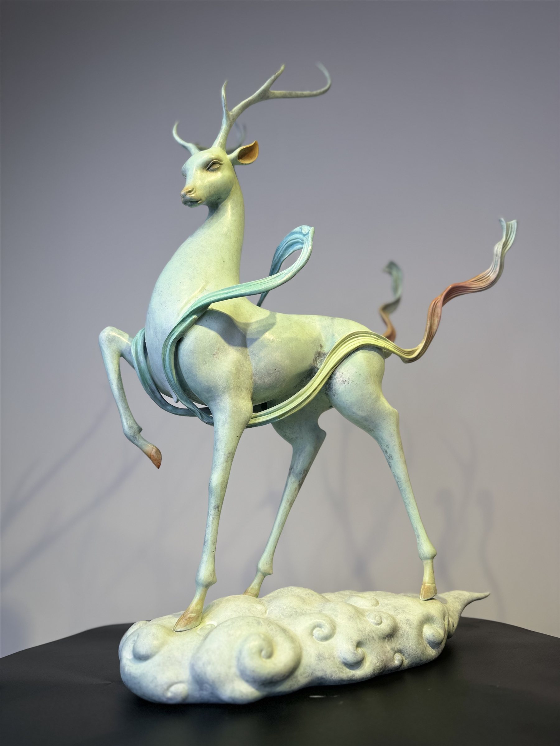 Patinated bronze sculpture of a slender antlered deer standing on a cloud-form base