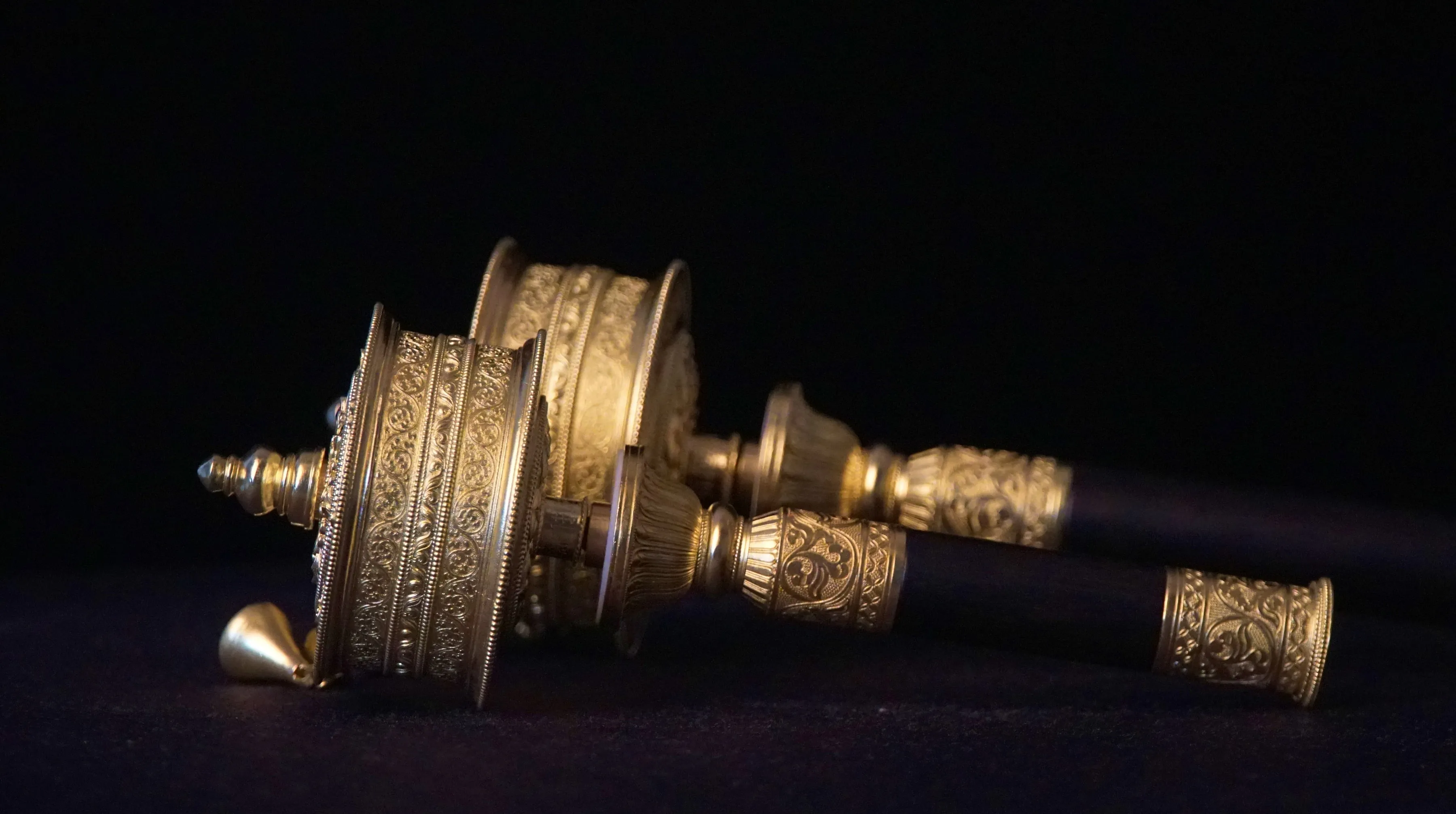 Three handheld Buddhist prayer wheels in brass, copper, and silver-plated finishes with dark wooden handles