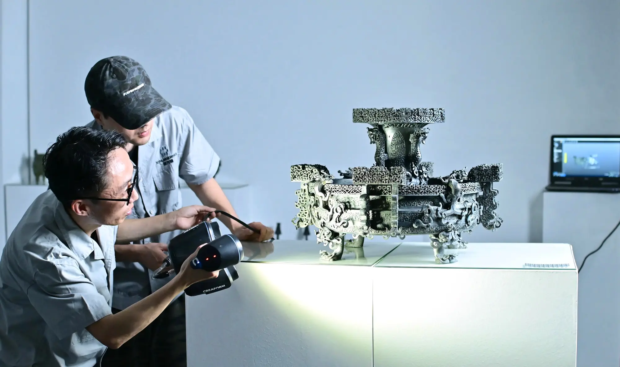 Technicians capturing the surface of an ornate bronze artefact with a handheld 3D scanner.