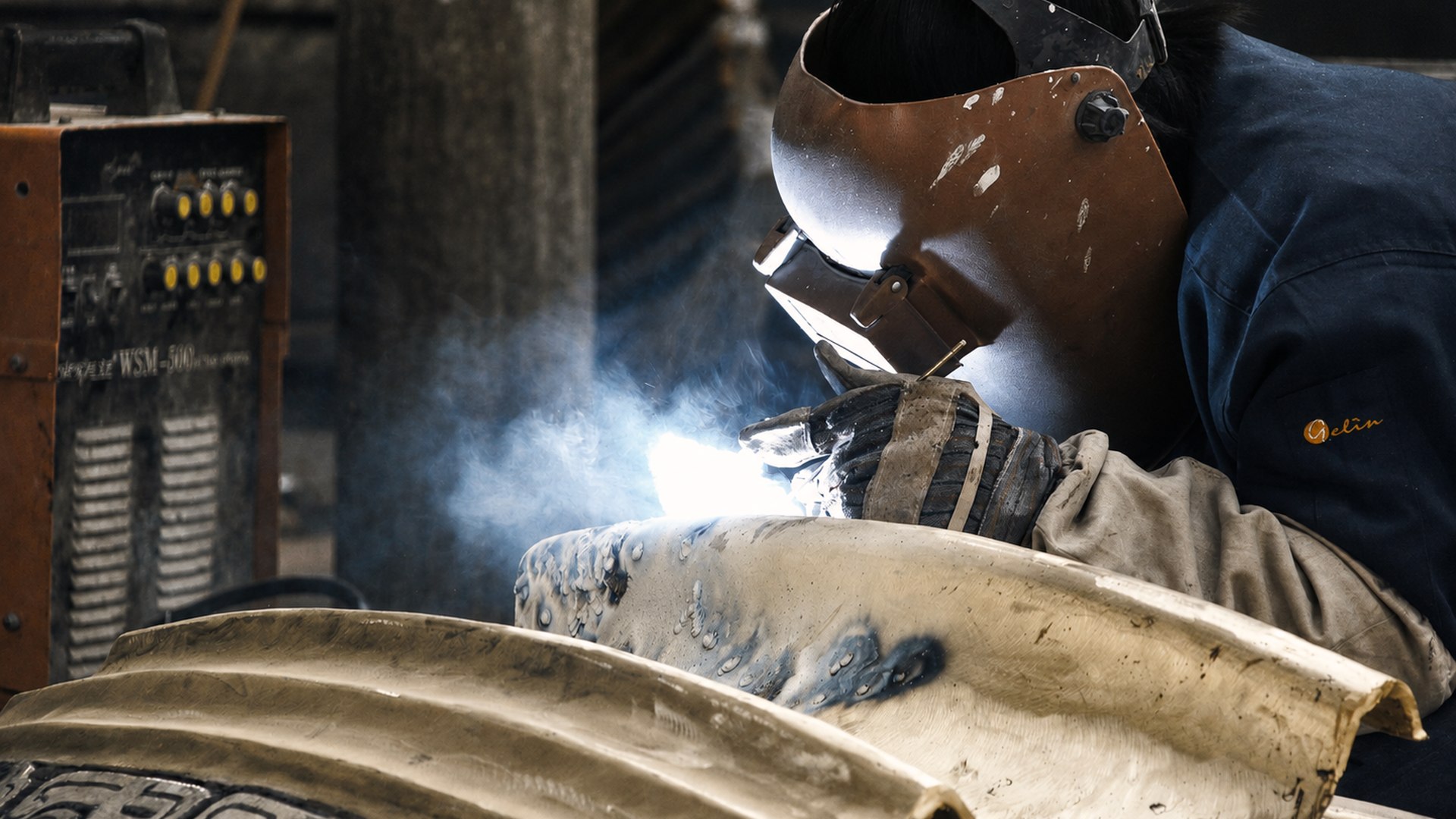 Welder joins an ornate metal section during assembly.