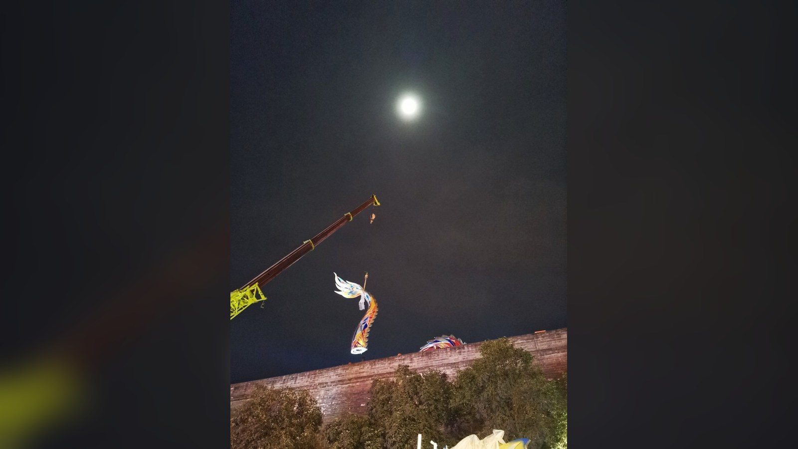 Crane lifting a curved decorative component during night-time installation.