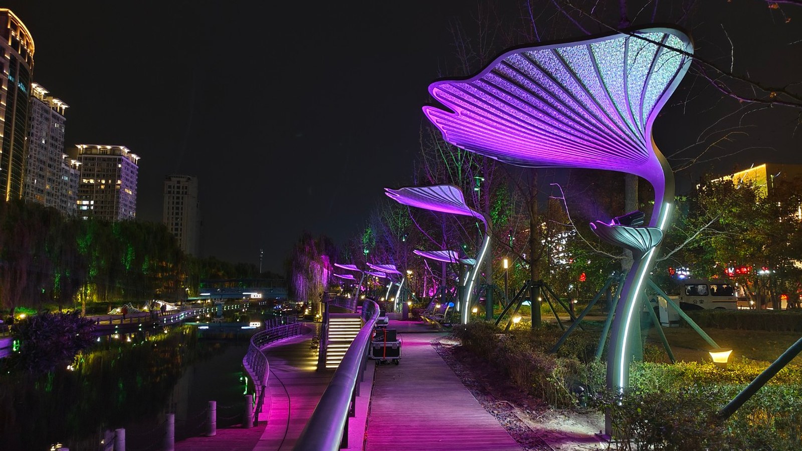 Illuminated sculptural structures along a waterside walkway at night.