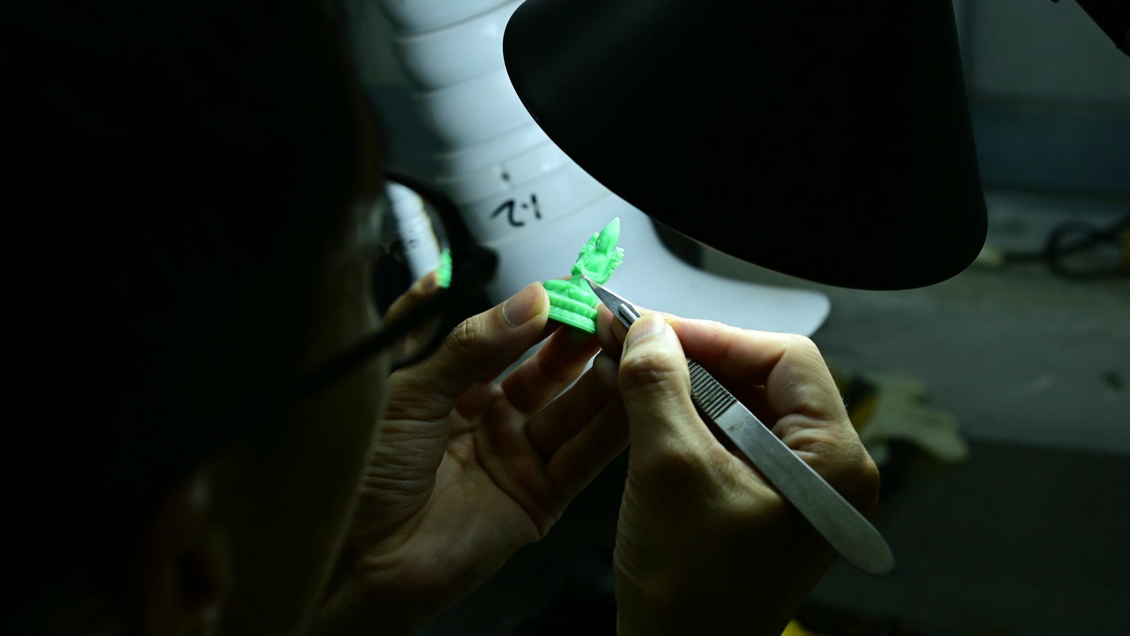 A craftsperson refining the details of a small wax model by hand.