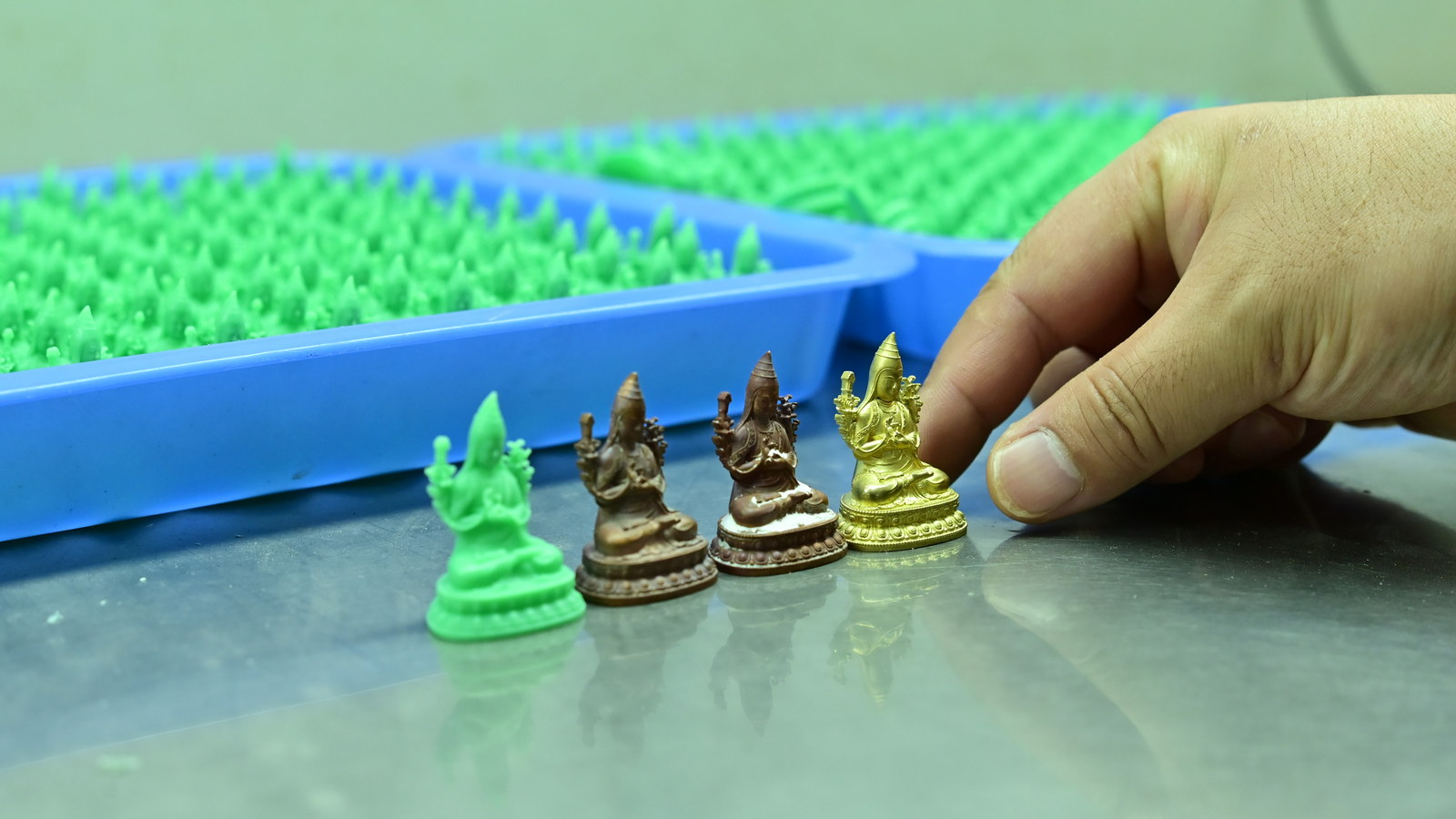 Small wax and metal figurines displayed beside a hand, showing their scale and sculptural detail.