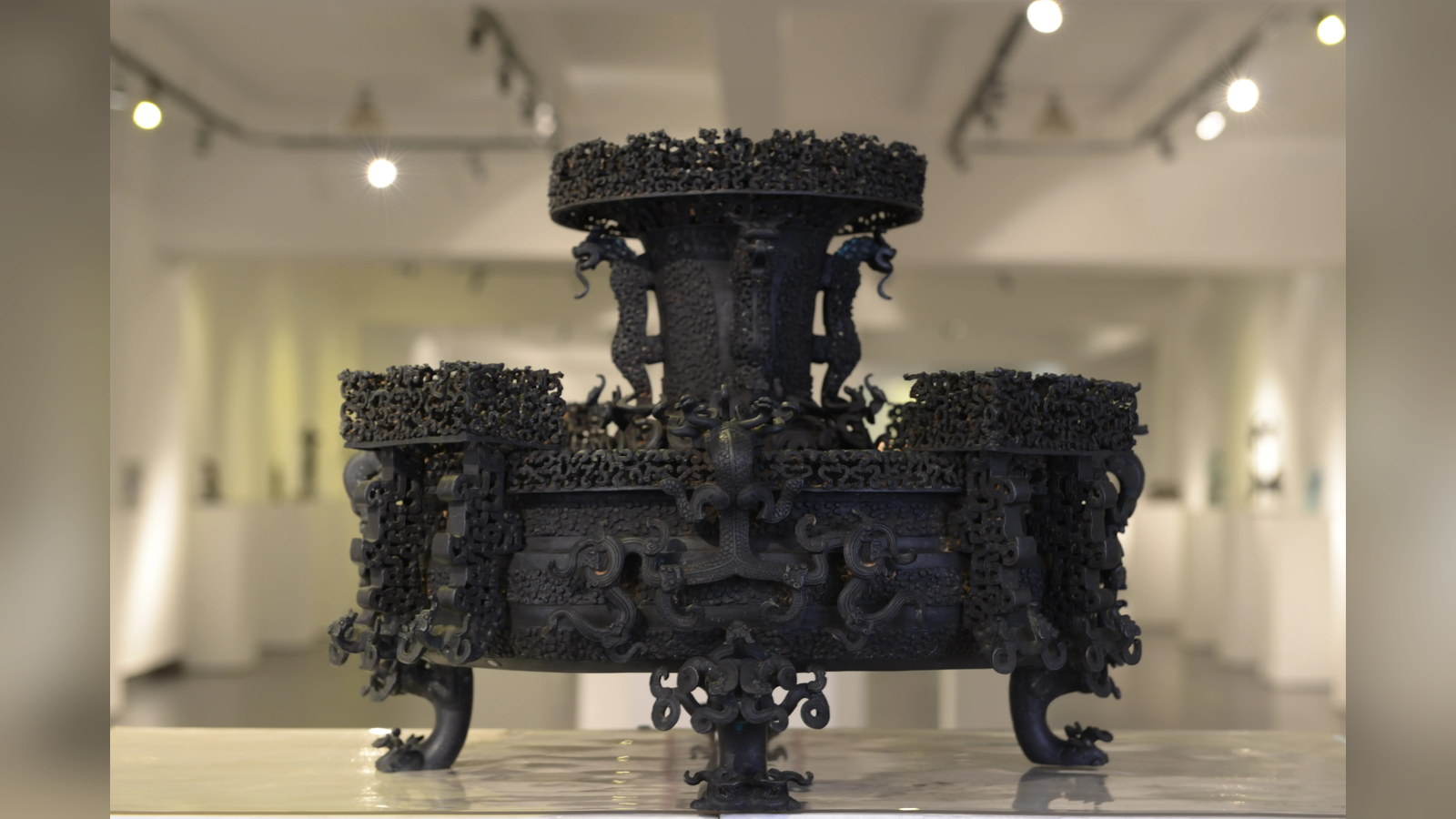An ornate bronze vessel replica displayed with intricate openwork decoration and sculptural supports.