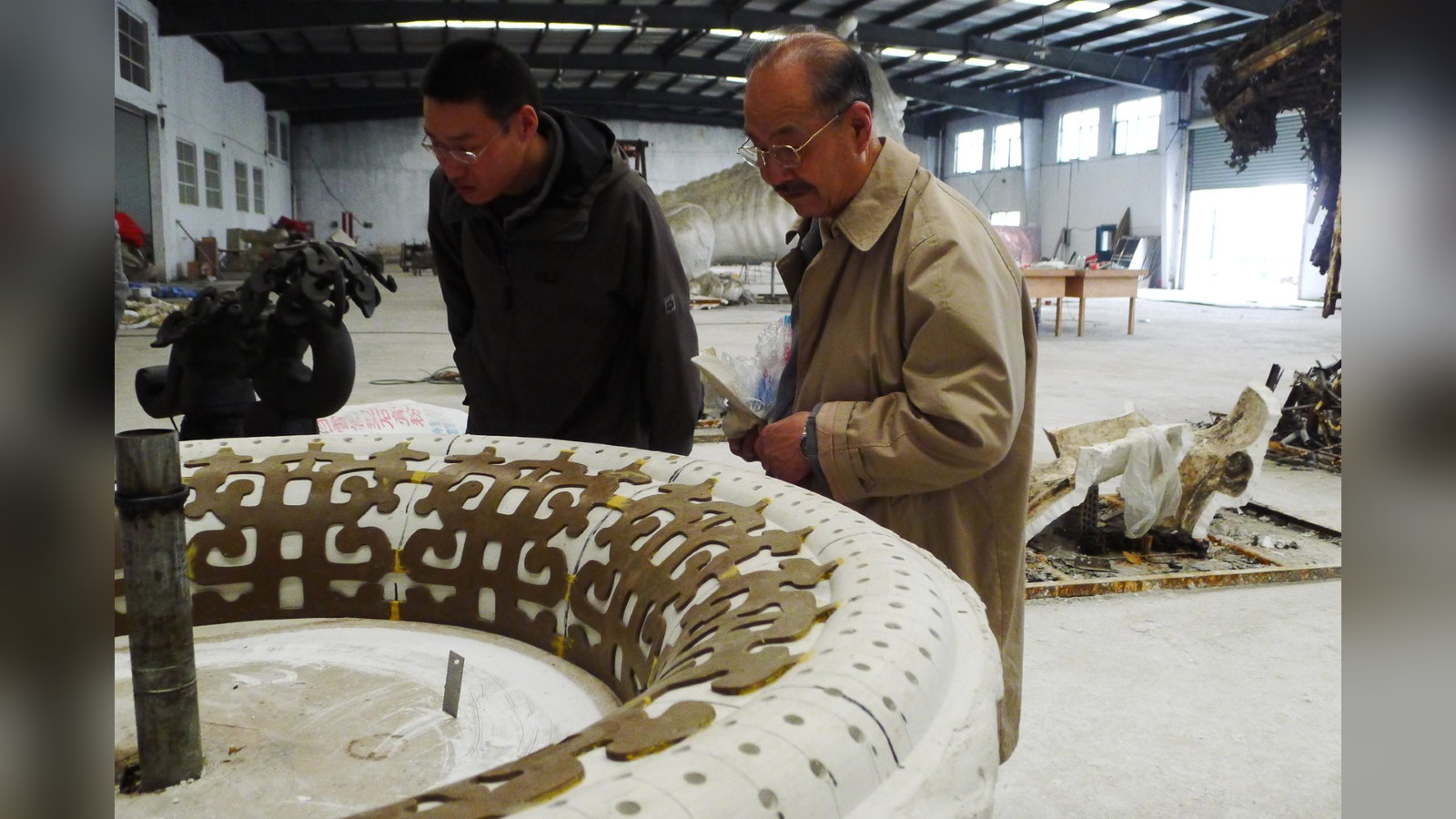 Two people examining a large patterned vessel form in a workshop.
