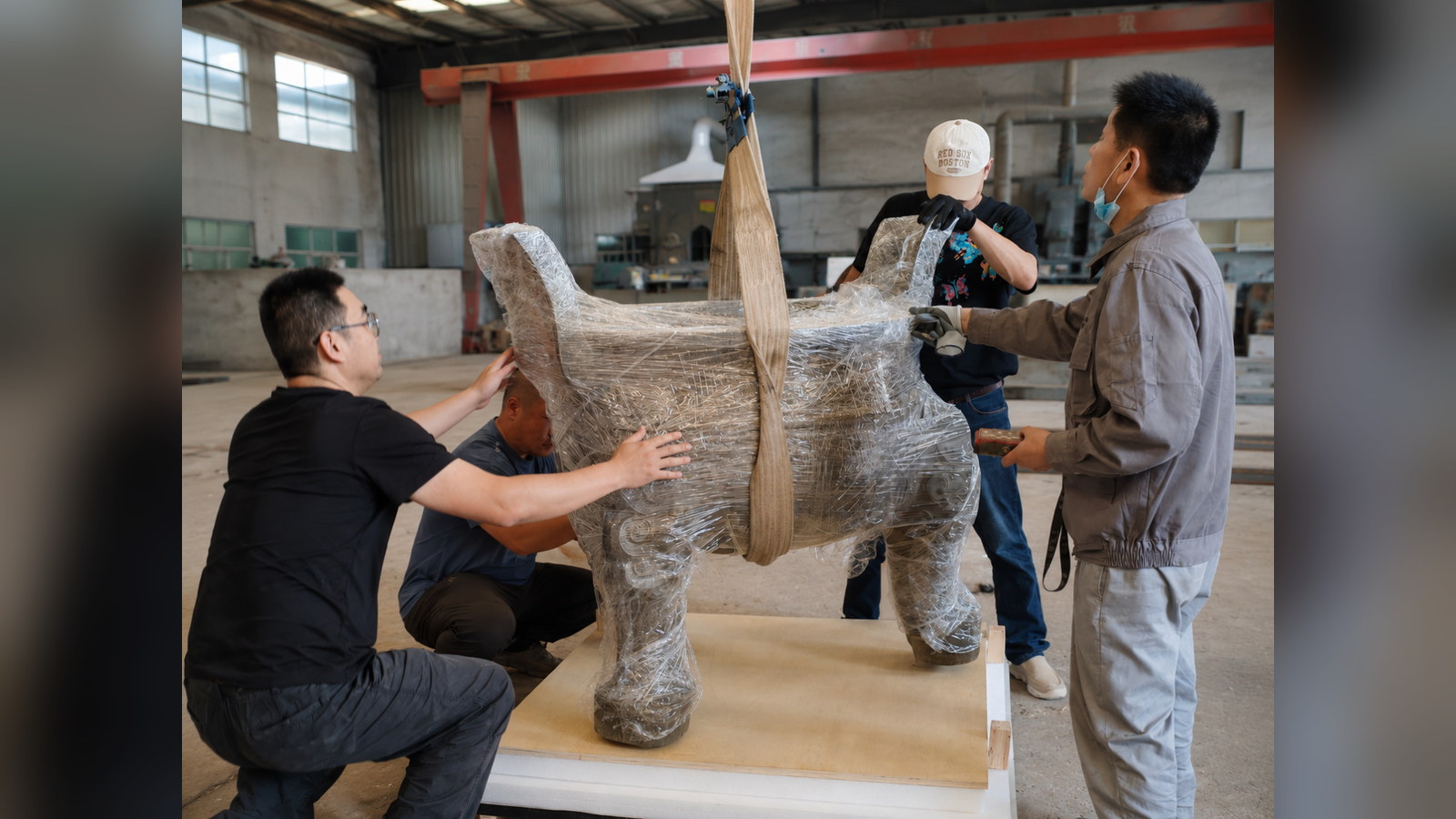 Workers guiding a wrapped vessel onto a lined crate base using lifting straps.