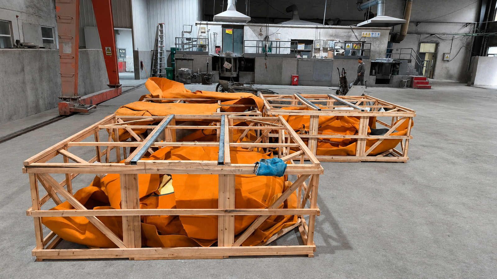 Large covered components enclosed in fitted timber frames on a workshop floor.