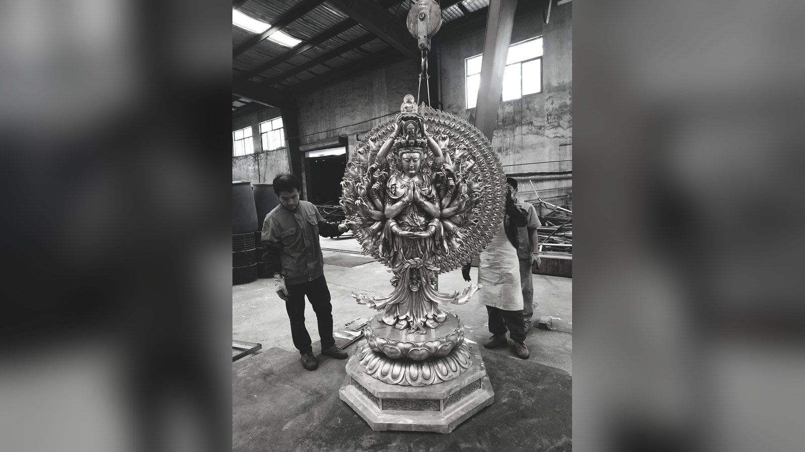 Workers guiding an ornate sculpture suspended from a workshop hoist.