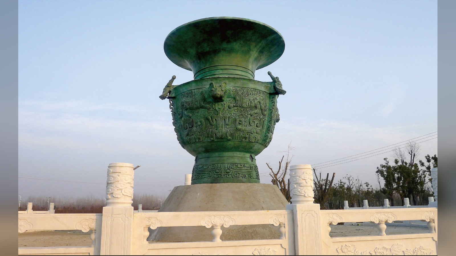 A completed large bronze vessel standing on a plinth within a landscaped setting.