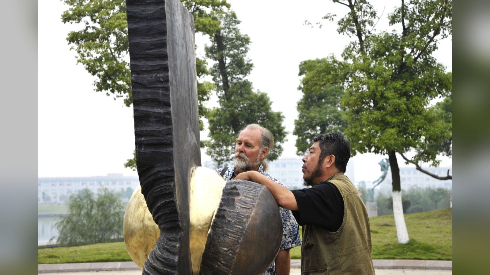 Two people examining details of an outdoor metal sculpture.