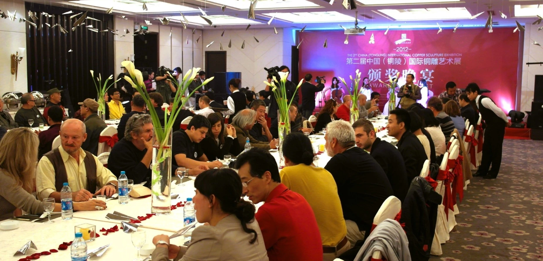 Guests talking around long tables at an exhibition banquet.