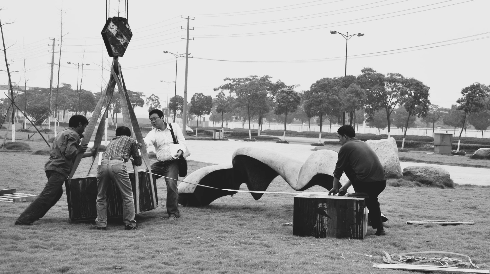 Black-and-white photograph of workers positioning a sculpture using lifting equipment.