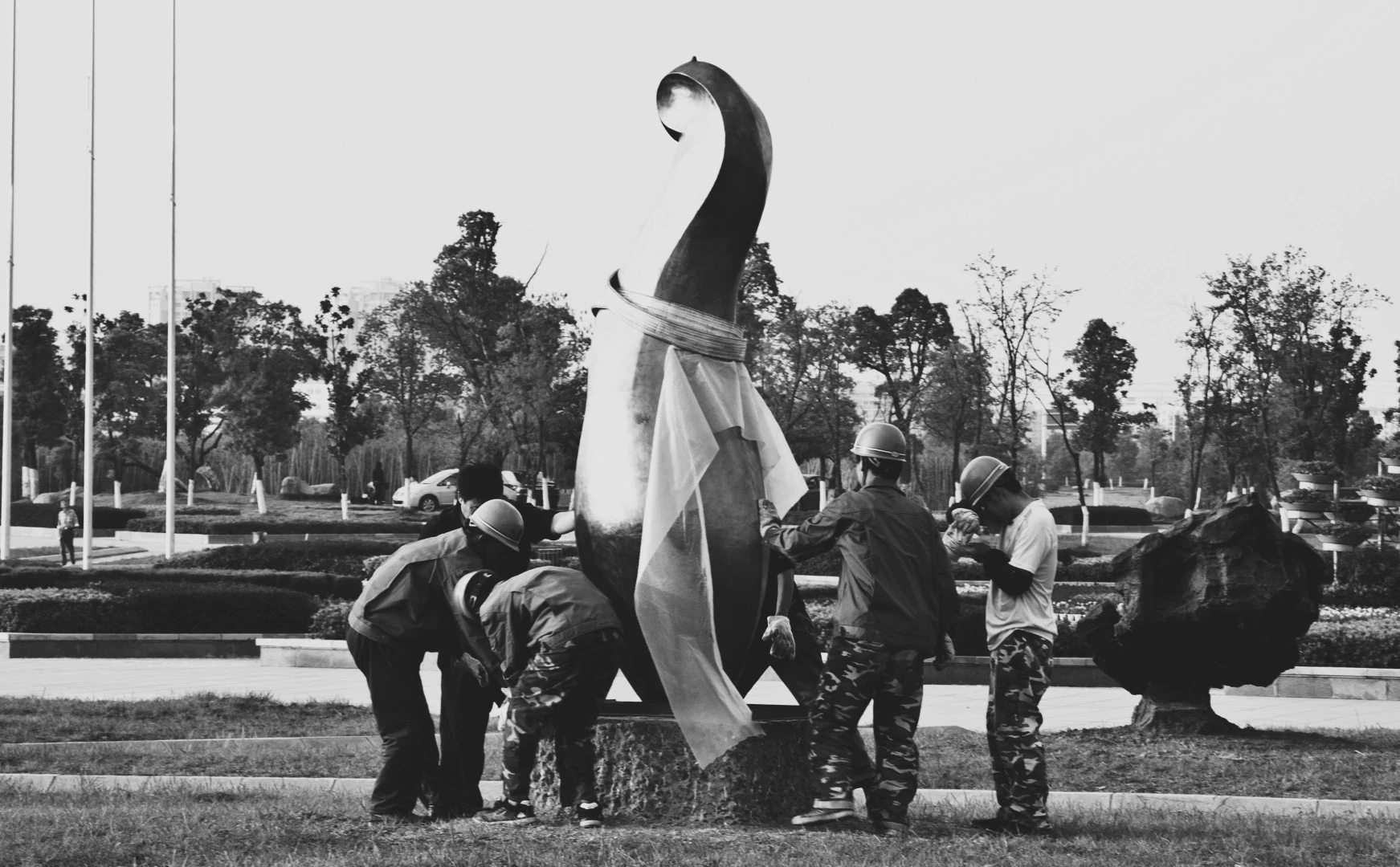 Black-and-white photograph of workers installing a sculpture on its base.