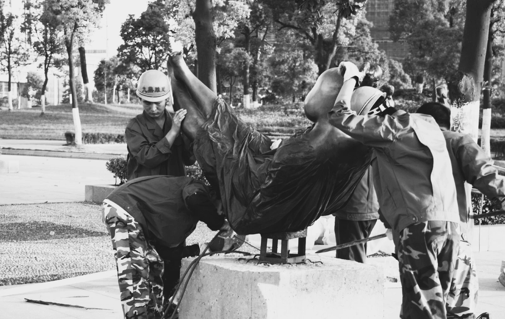 Black-and-white photograph of workers securing a wrapped sculpture at its installation site.