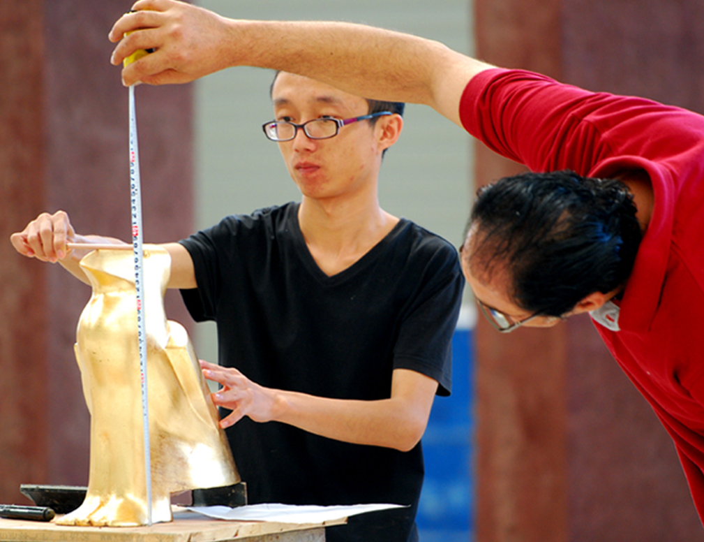 A sculpture model is measured with a tape measure.