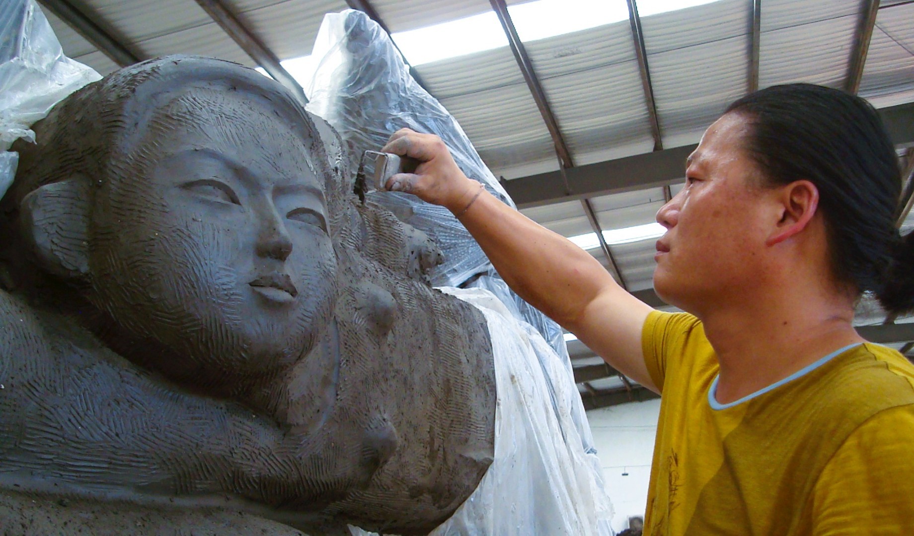 An artist works on the face of a large clay sculpture.