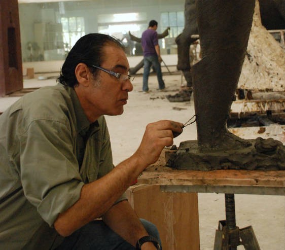 An artist works on a sculpture model at a workshop table.