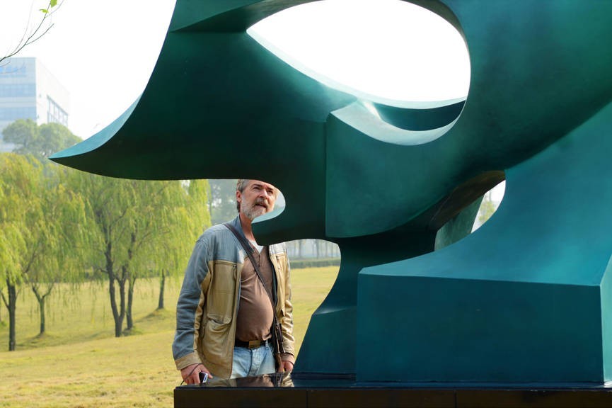 A participant stands beside a large green abstract sculpture.