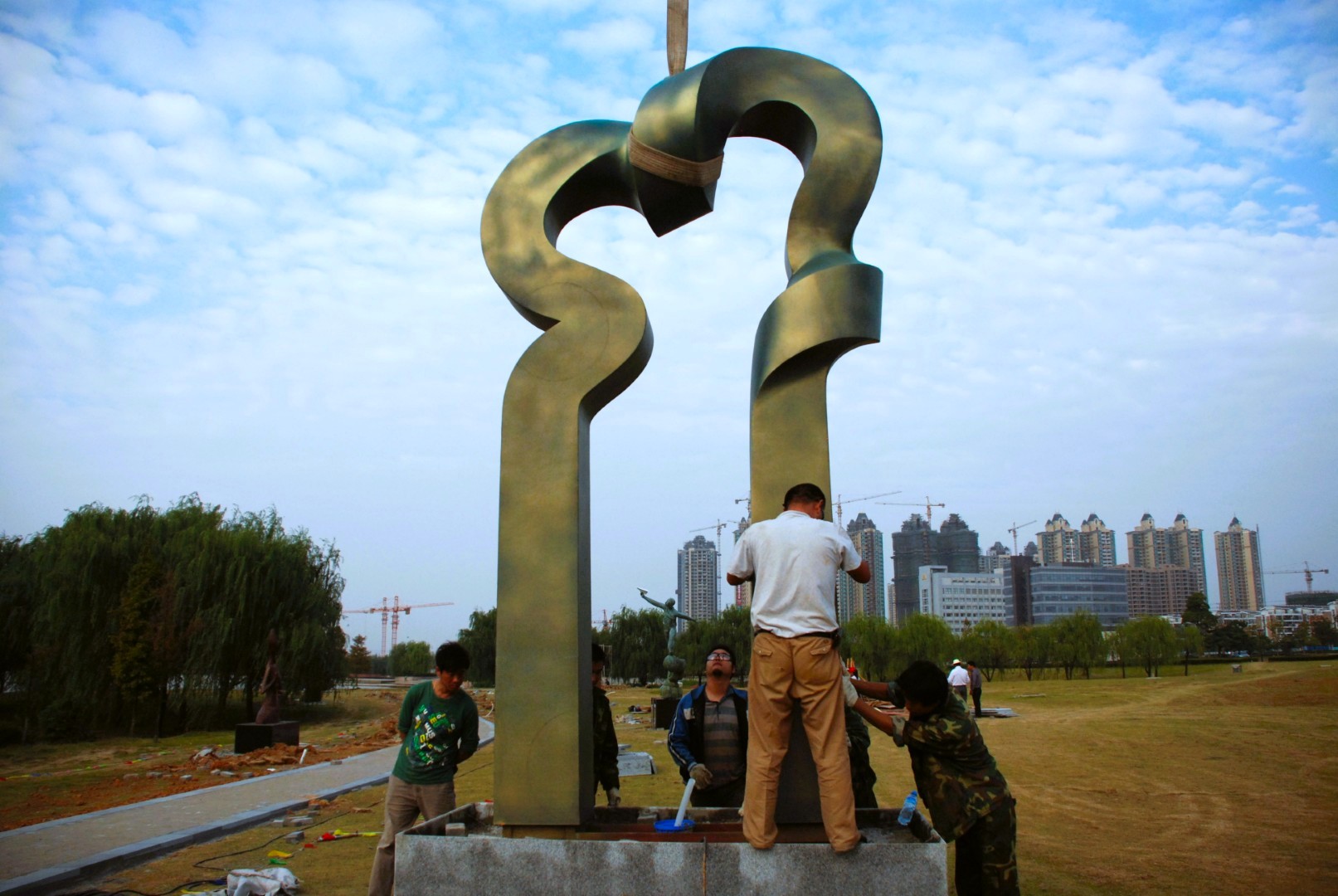 Workers attend to the base of an upright sculpture during installation.