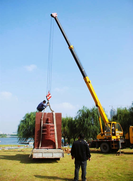 A crane lifts a tall sculpture during outdoor installation.