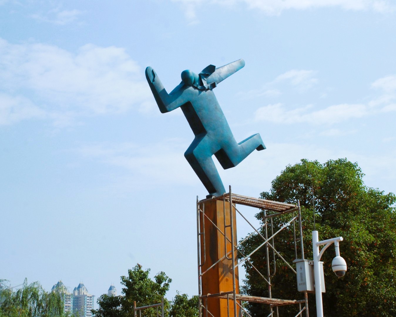 Scaffolding surrounds the support of a green figurative sculpture.