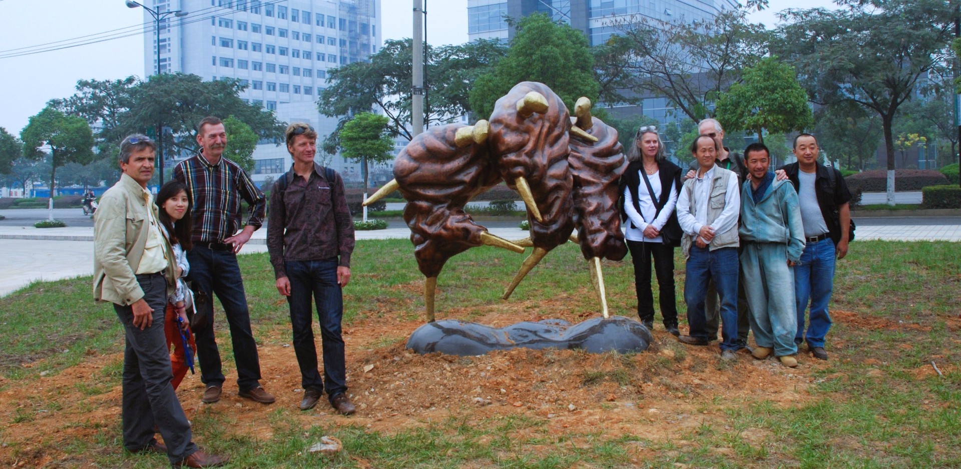 Participants gather beside an outdoor bronze sculpture with gold-coloured details.