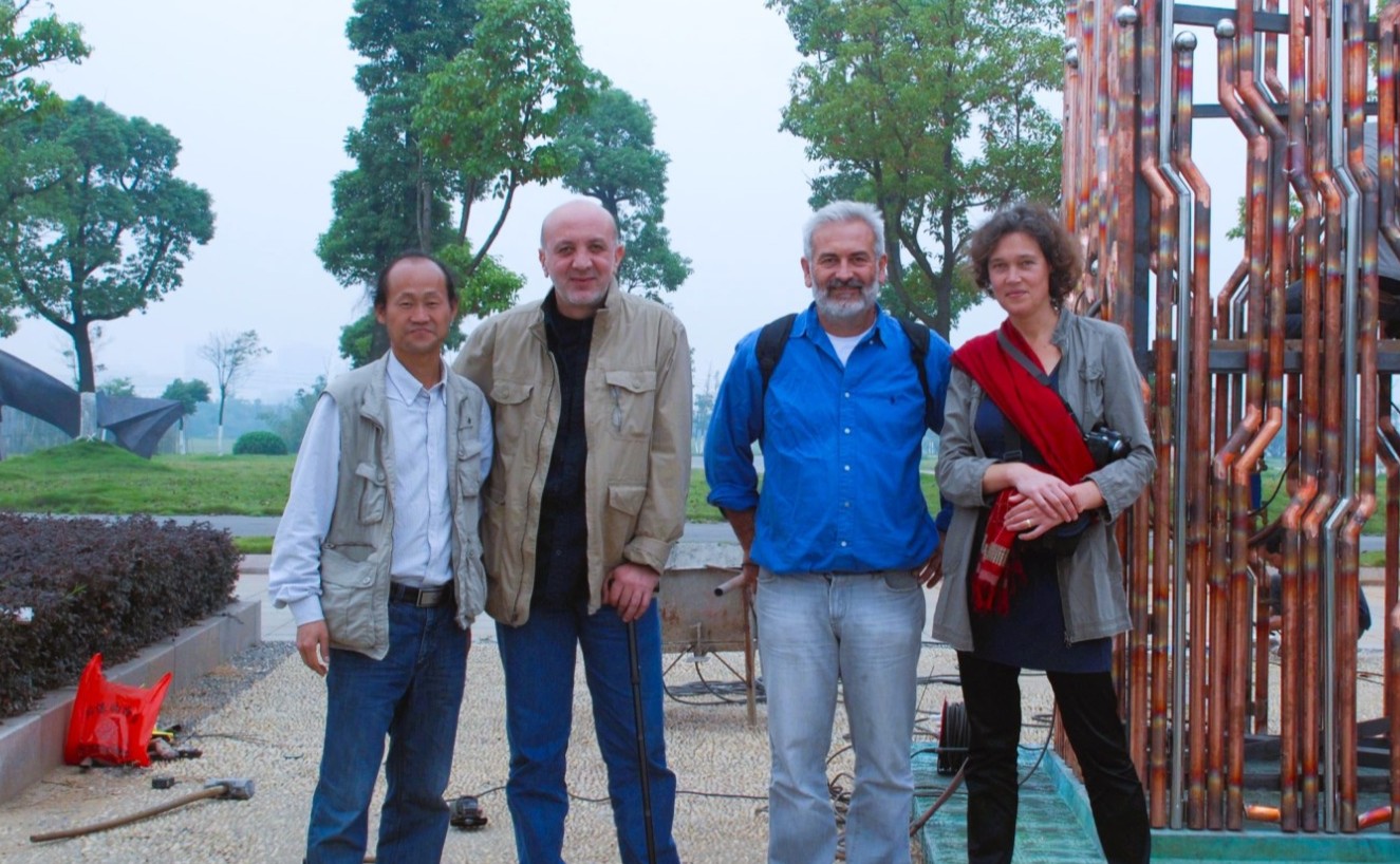 Four participants stand beside a sculpture made from copper-coloured tubes.