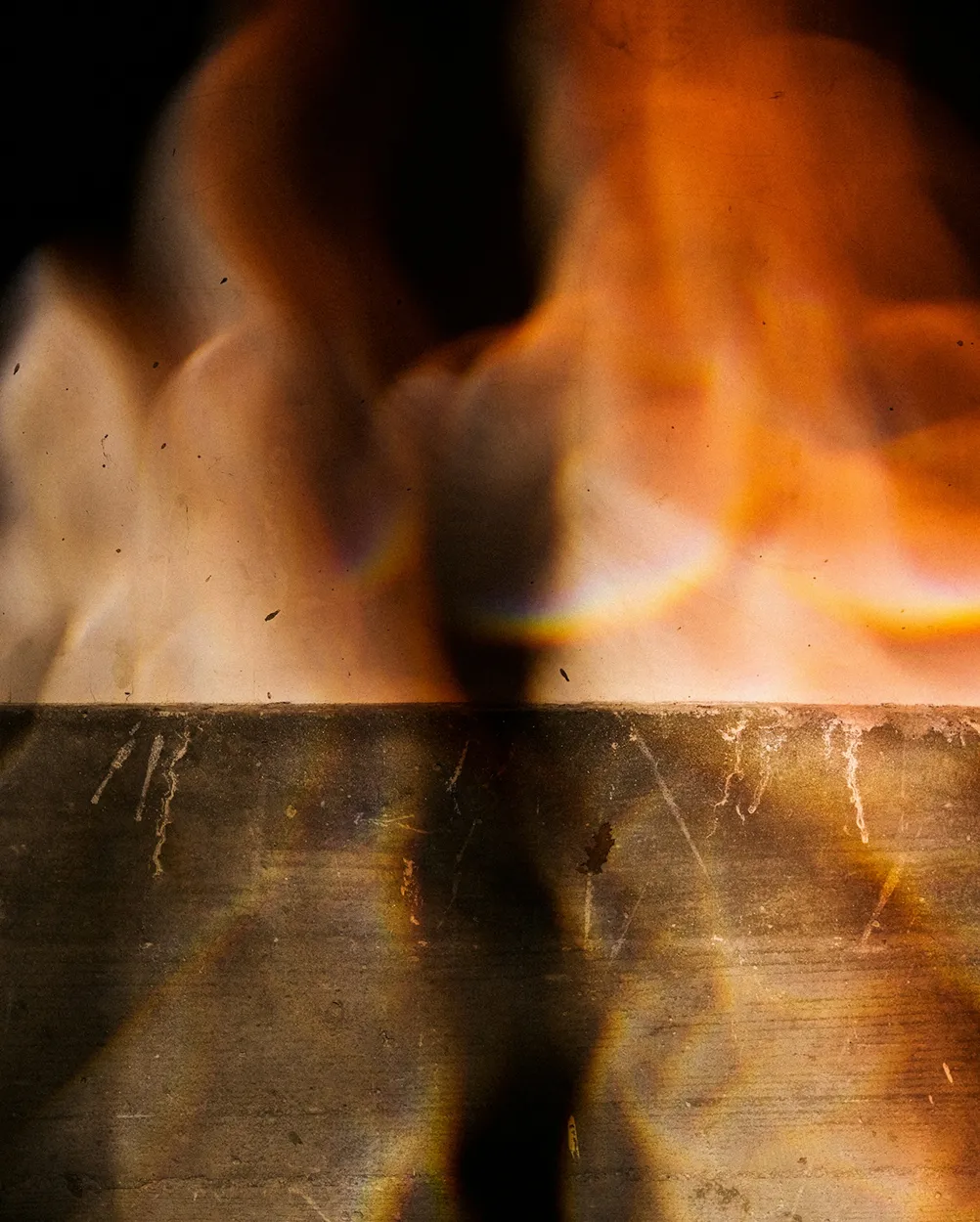 Close-up of orange and yellow flames burning on a dark metal surface.