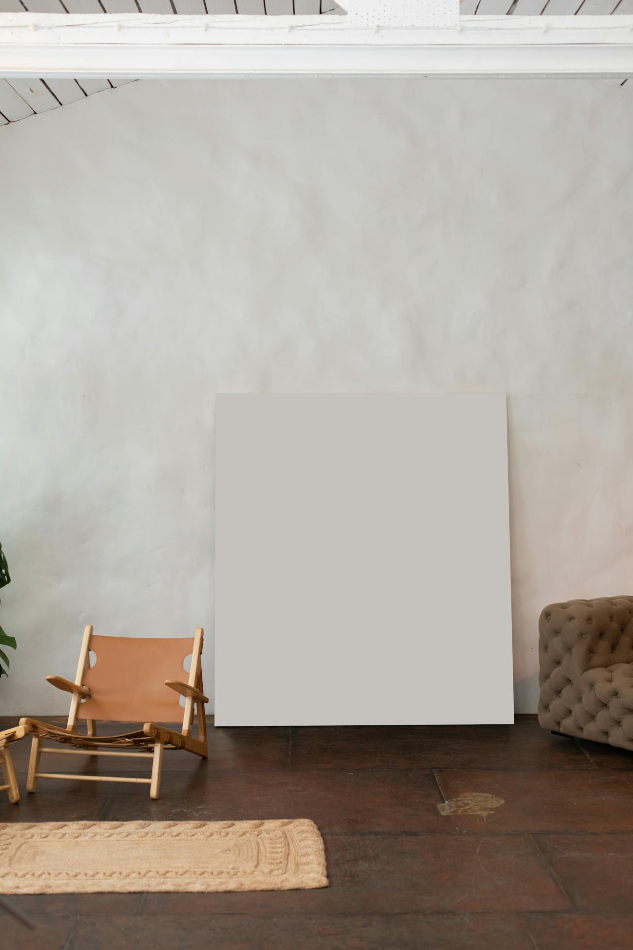 Modern room with blank square canvas on floor between a leather chair and a tufted sofa.