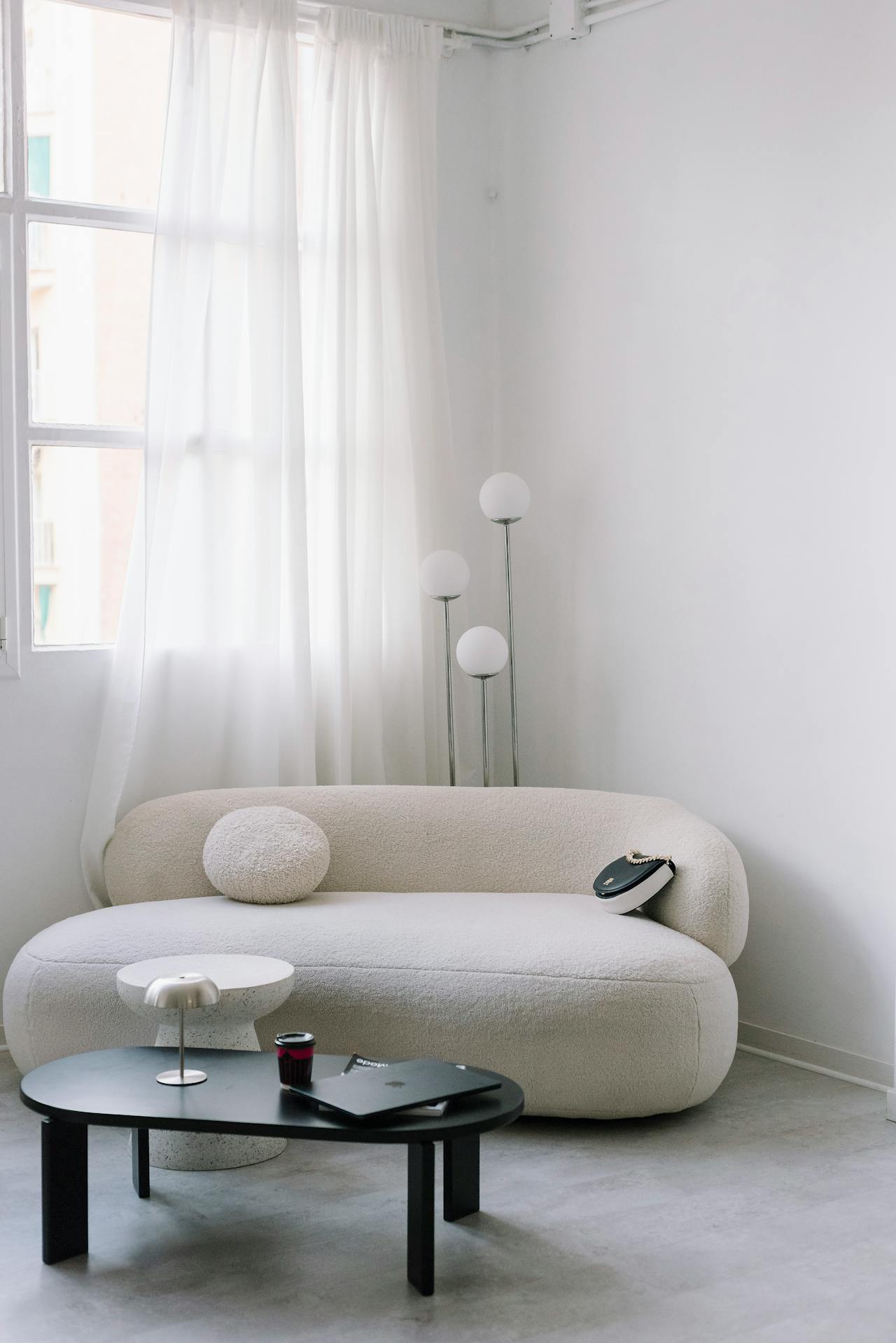 Minimalist living room with a curved white sofa, round pillow, black coffee table, and floor lamp.