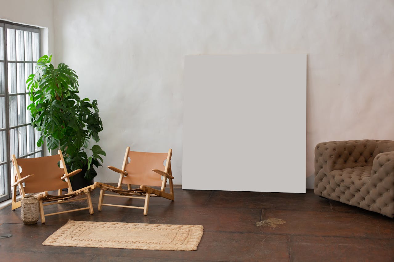 Minimalist room with two wooden lounge chairs, a large plant, blank canvas, and tufted sofa.