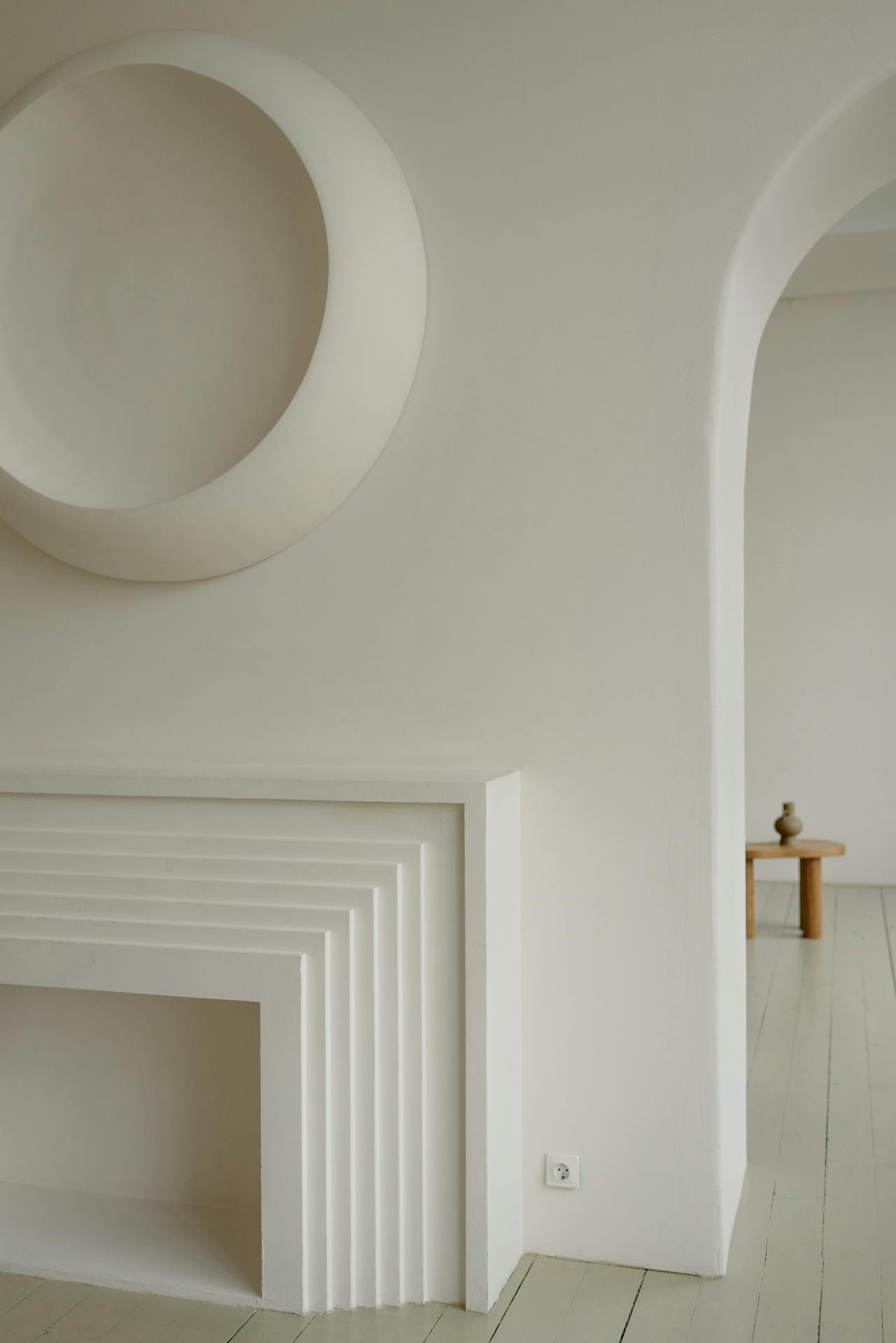 Minimalist white interior with layered geometric fireplace and round wall decoration.