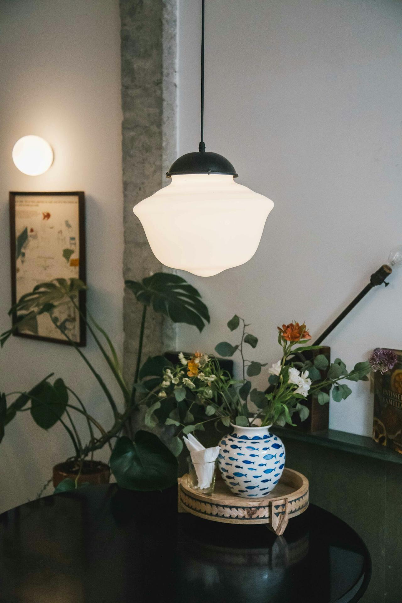 White pendant lamp over table with vase of flowers and green plants in cozy indoor setting.