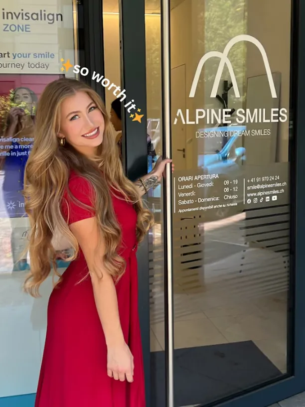 Giovane donna in abito rosso sorride davanti all'ingresso della clinica dentale Alpine Smiles a Lugano, zona Invisalign.