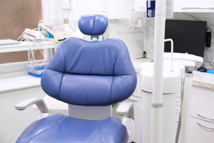 Blue dental chair with headrest in a clean dental clinic room.