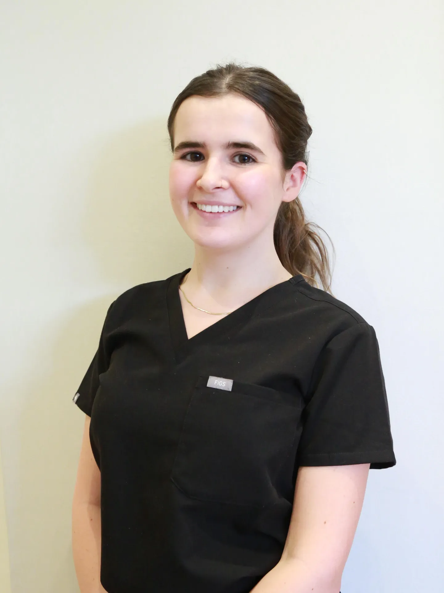 Smiling woman with brown hair in a black scrub top against a light background.