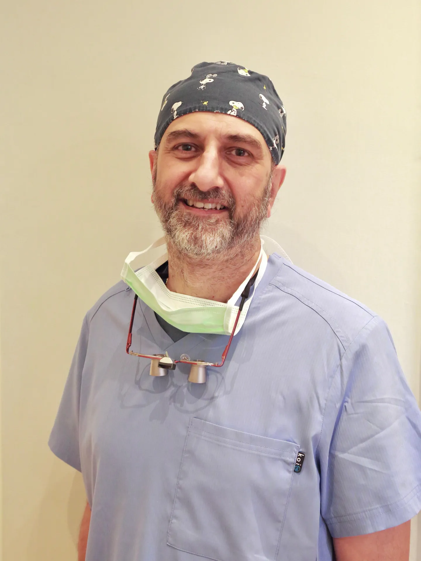 Smiling male medical professional wearing light blue scrubs and a Snoopy surgical cap.