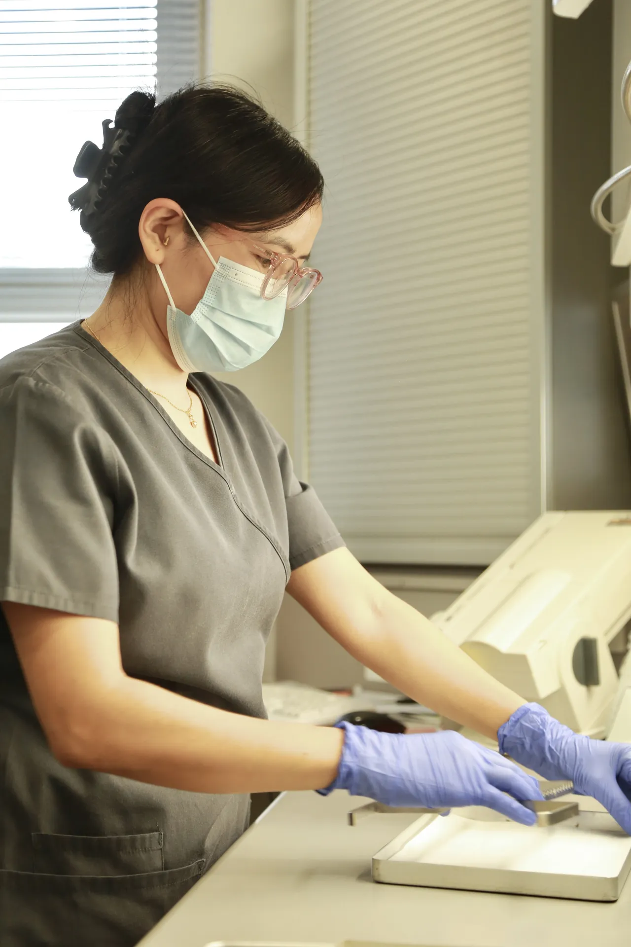 Healthcare worker in mask and gloves handling equipment on a medical workstation.