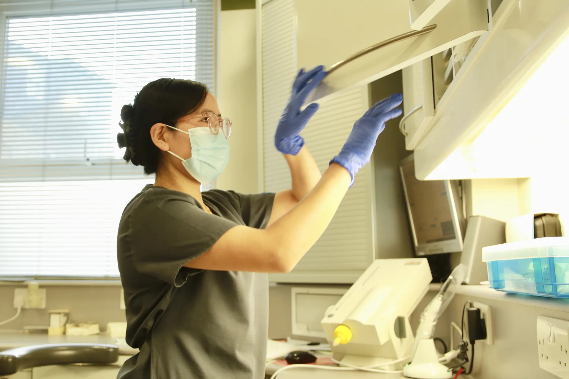 Person wearing mask and gloves reaching to open a cabinet in a clinical or laboratory setting.