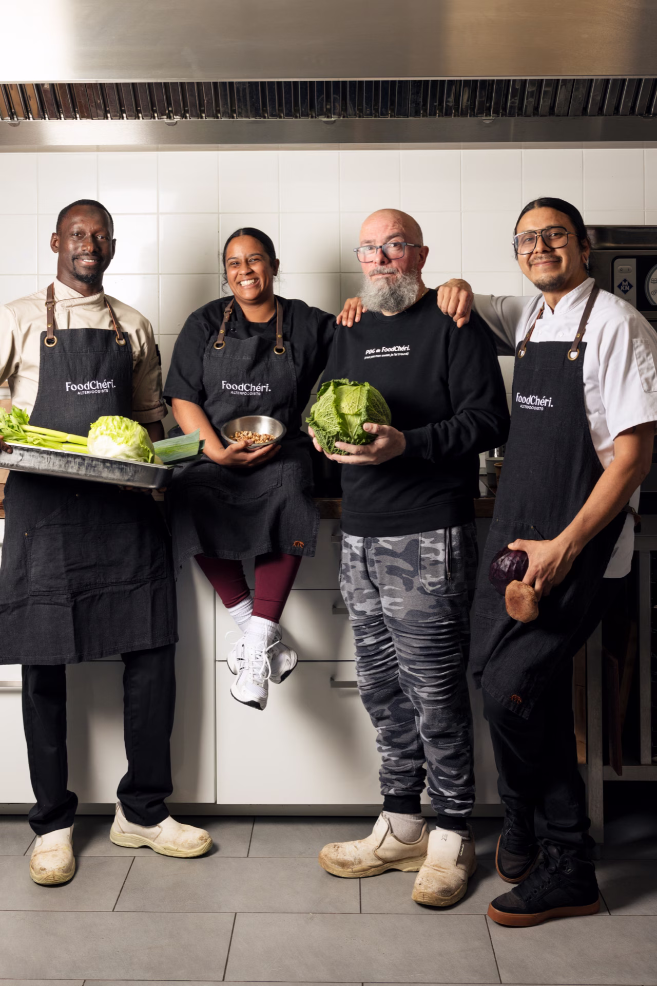 Quatre chefs debout dans une cuisine professionelle, portant des tabliers FoodChéri avec légumes et noix.