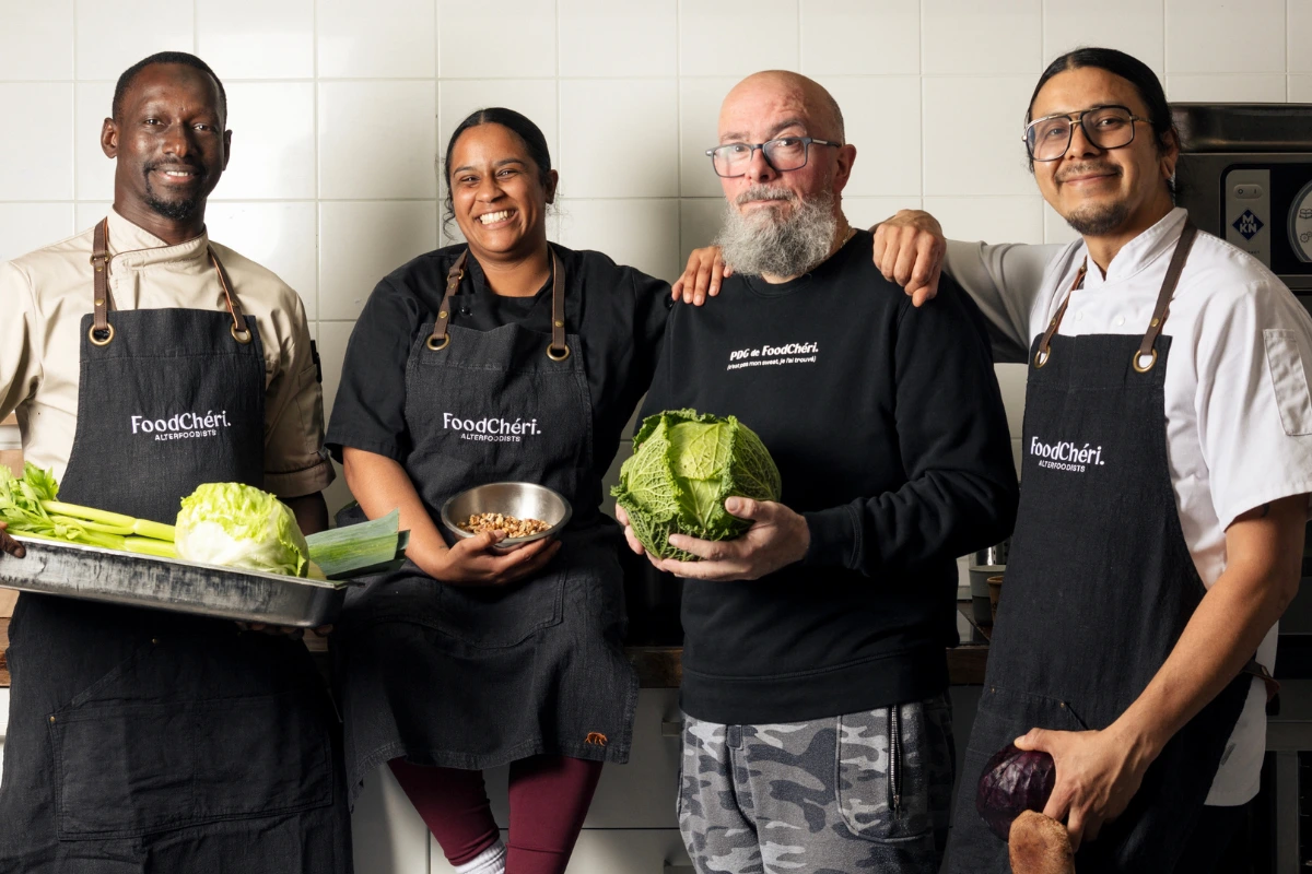 Quatre chefs souriants portant des tabliers FoodChéri avec des légumes frais en cuisine.