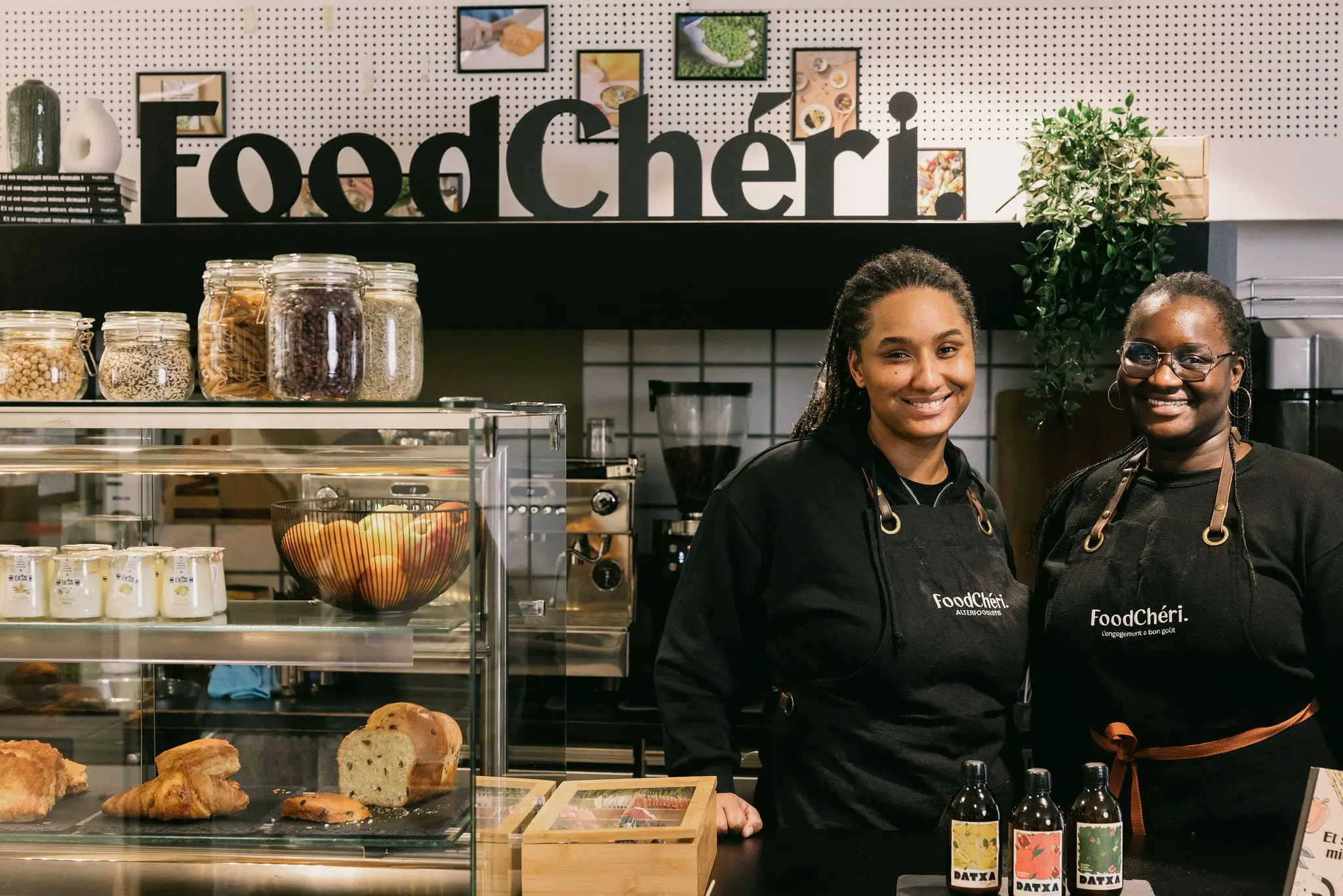 Deux femmes souriantes en tabliers FoodChéri dans une boutique avec pâtisseries et bocaux alimentaires.