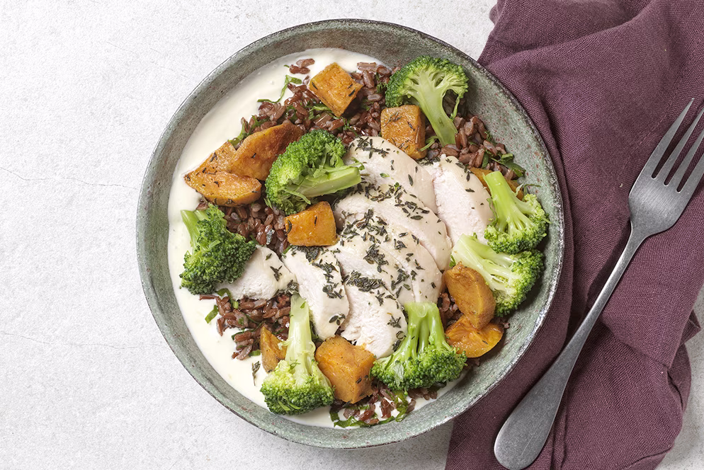 Assiette avec poulet tranché, brocoli, courge rôtie, riz rouge et sauce blanche, avec fourchette et serviette.