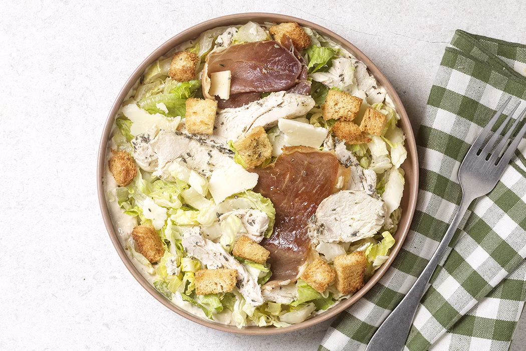 Salade César avec laitue, poulet, croûtons, tranches de jambon et copeaux de fromage.